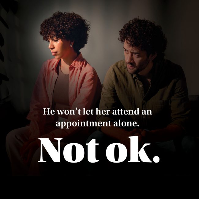Poster text reads “He won’t let her attend an appointment alone. Not ok.” — campaign on controlling behaviour.